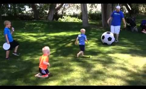 Father kicks large soccer ball knocking down boy