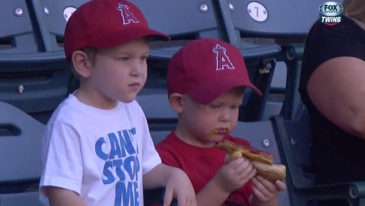 Kid struggles to eat hot dog at baseball game